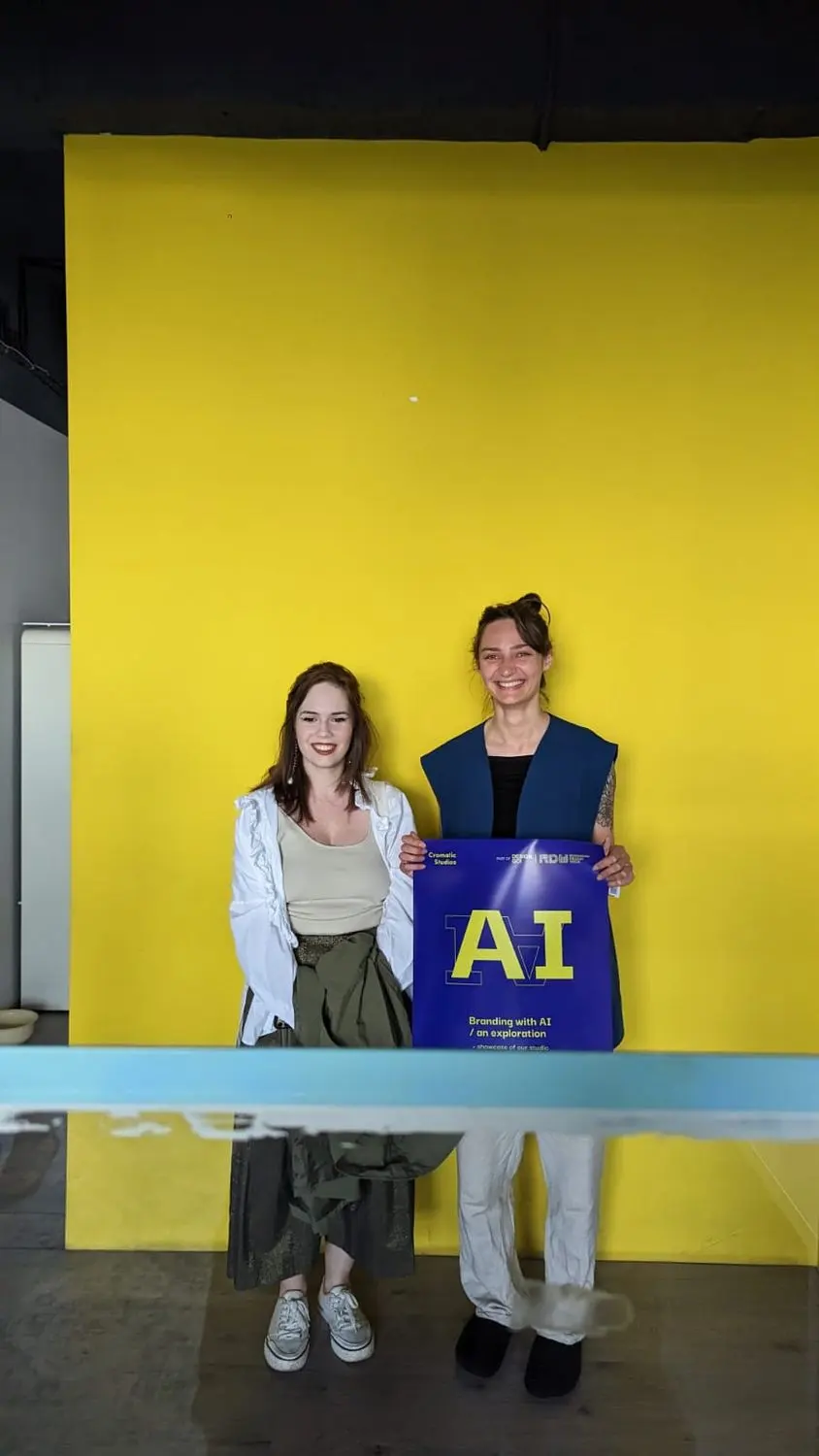 Two visitors with an AI tote bag against the yellow wall