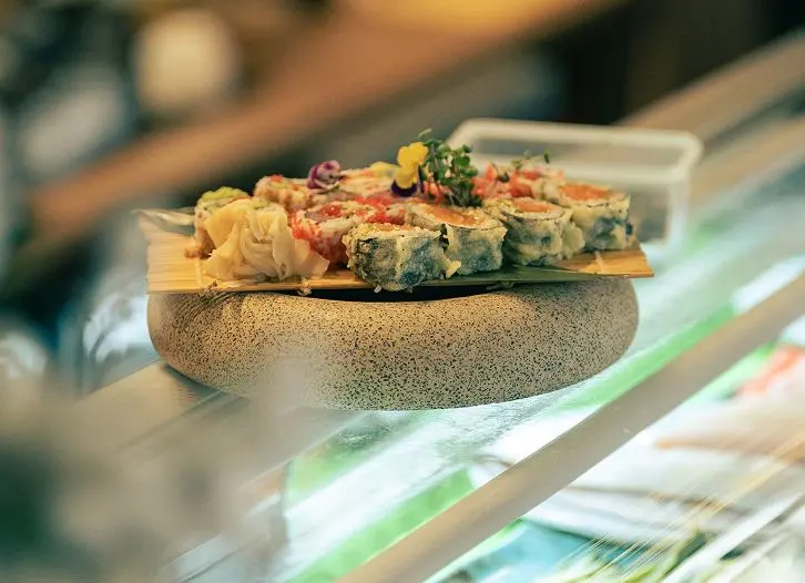 Rulouri de sushi pe un platou de piatră, lângă tejghea