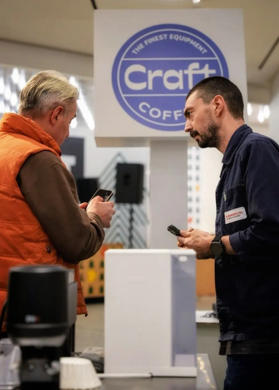 A visitor and a team member in front of the Craft Coffee badge