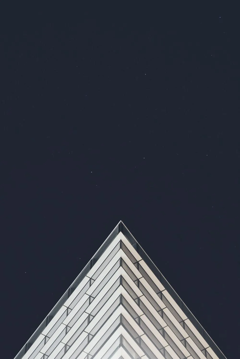 The tip of a glass building, rising into a dark sky
