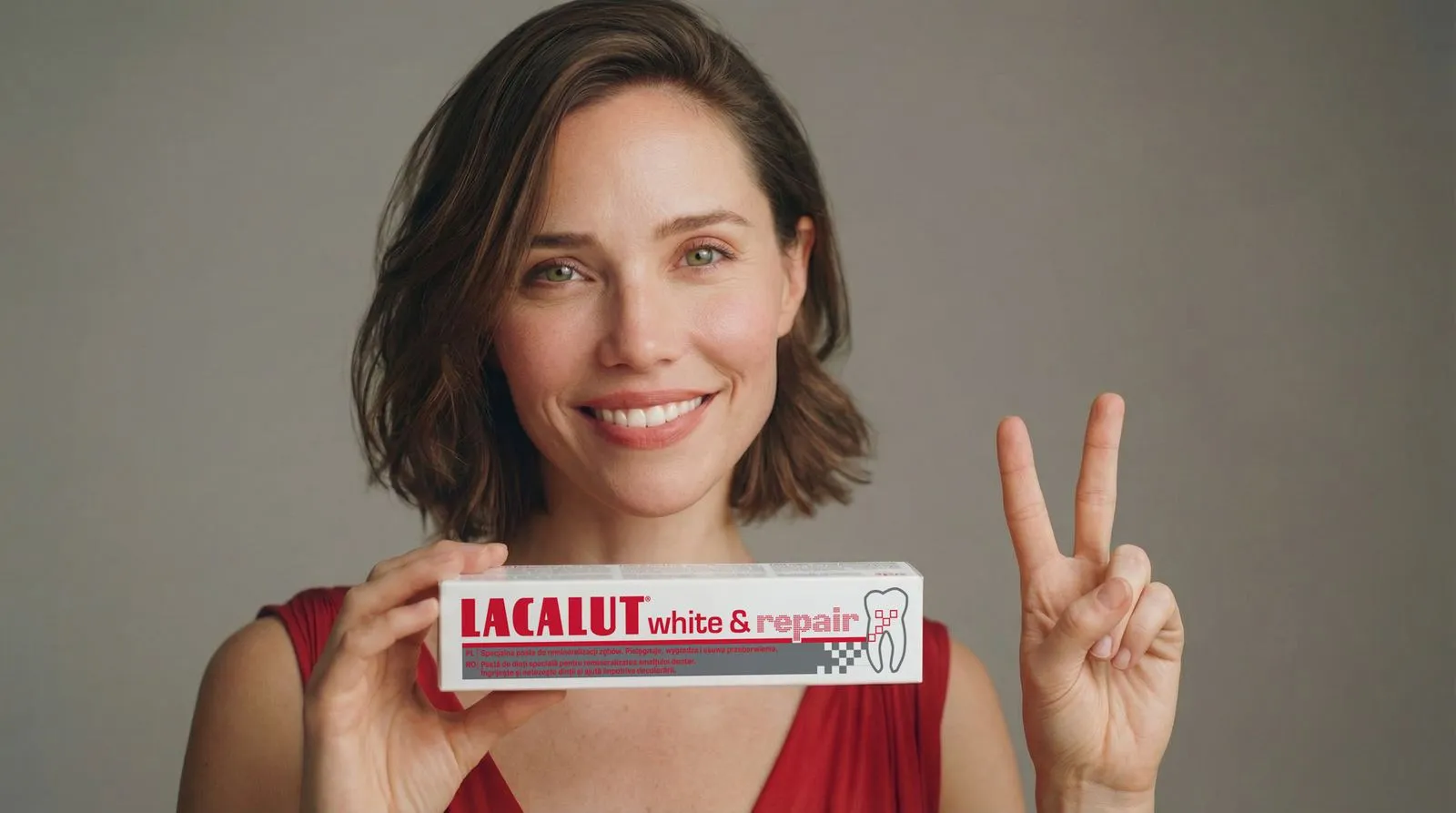 A woman in a red dress smiles and holds up a tube of Lacalut White & Repair, her other hand making a V