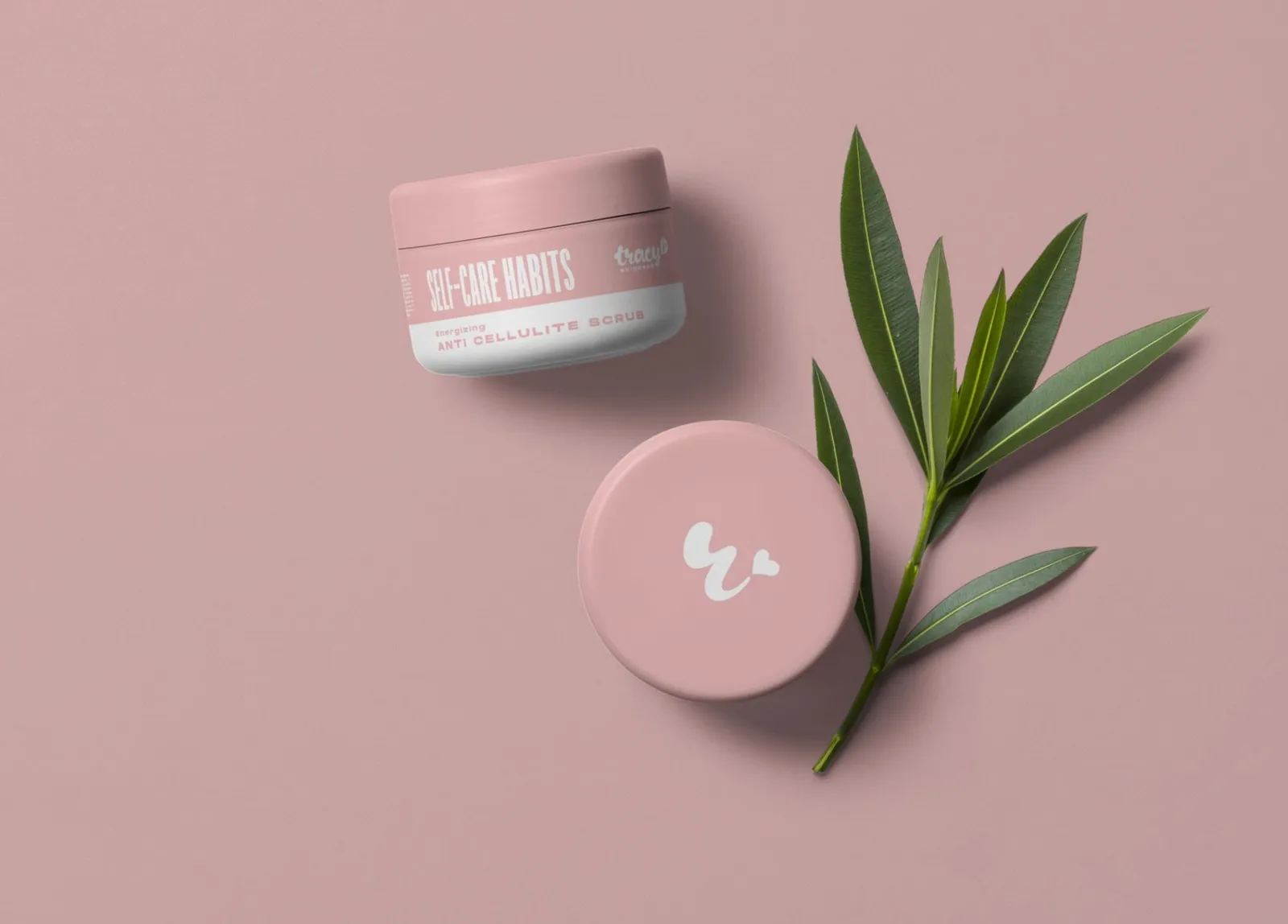 Un borcan roz Self-care Habits și capacul lui cu monograma, lângă o crenguță cu frunze