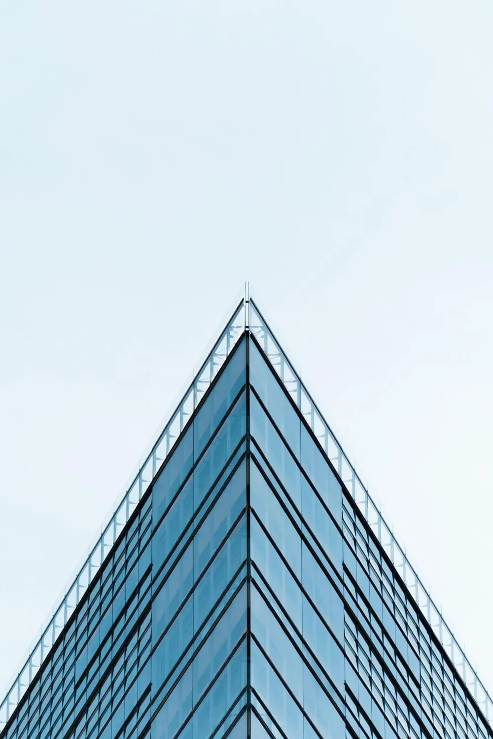 The tip of a glass building, rising into a light blue sky