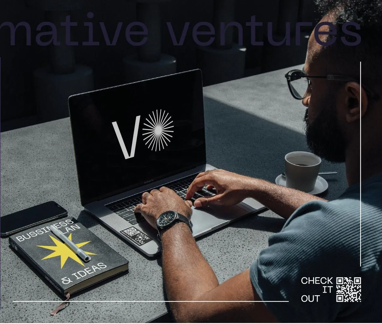 A man types on a laptop showing the V✳ logo, next to a notebook with a yellow star and a QR code